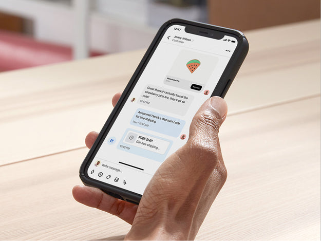 Business owner sits at her desk in her back office and uses Shopify Inbox to chat with a customer on her mobile device. She shares a discount code in the chat to close the sale.